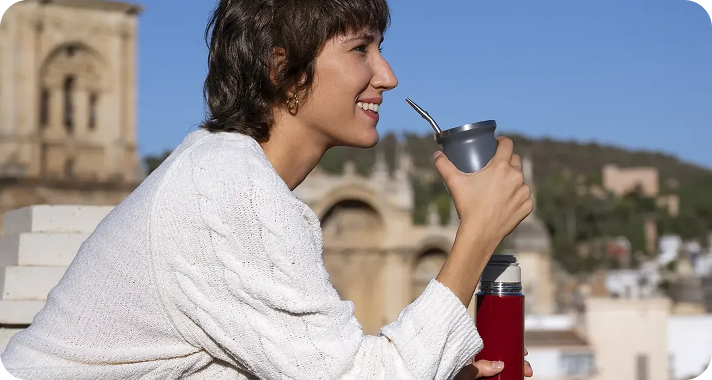 A woman drinking mate outdoors with a European village in the background