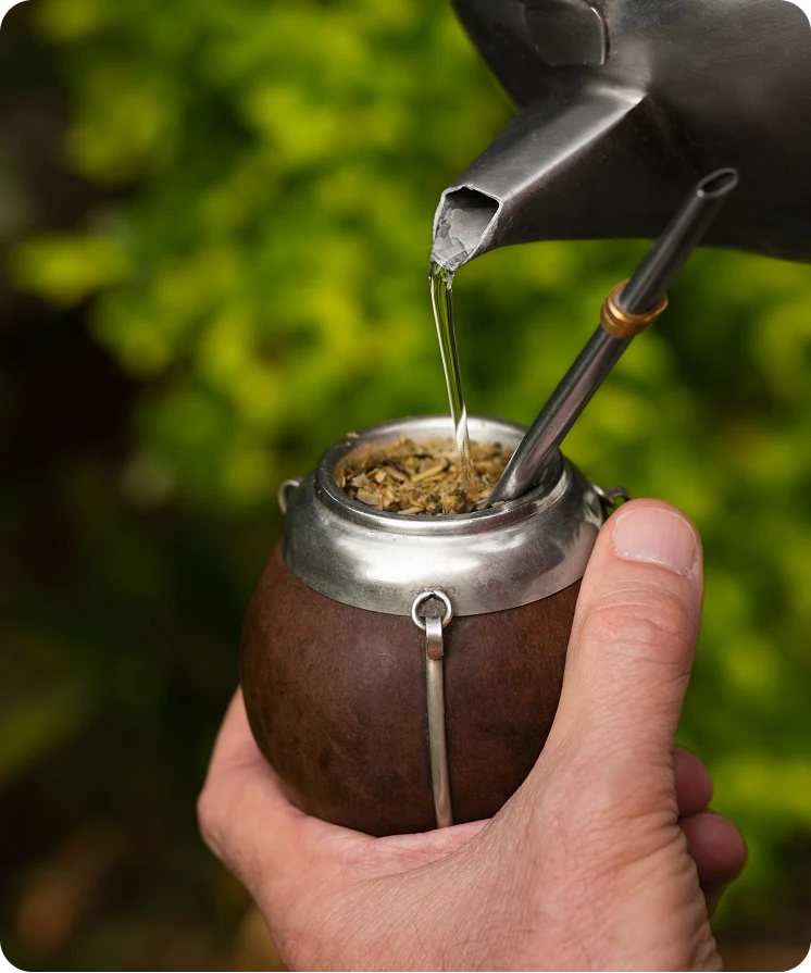 Hands pouring hot water into a mate gourd outdoors